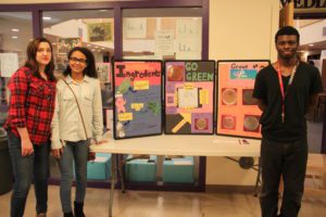 Three P-TECH students pose for a photo in front of their project display