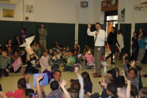 Principal Roy Stiles and room full of students raise their hands