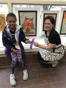 Female student and teacher in front of art work at art show.