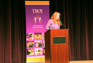 Nancy Jo Sales speaking behind a podium on stage at Troy Middle School.