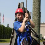 Male student in helmet and harness as he prepares for the ropes course