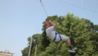Male student in helmet and harness swinging through the air at the ropes course of HVCC.