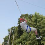 Male student in helmet and harness swinging through the air at the ropes course of HVCC.
