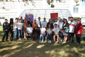 Large group of students, administrators and donors smile for the camera in front of the greenhouse at Troy High School