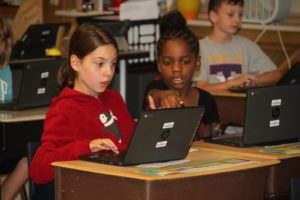 Two young girls working on laptops