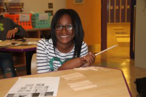 Girl smiles at camera while making a structure out of Popsicle sticks