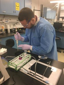 Justin Haviland in lab coat and gloves using lab instrument 
