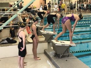 Girls at swim meet preparing to dive into the pool.