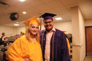 female student in yellow cap and gown with male student in purple cap and gown