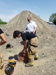 Student in fire gear picking up a fire hose