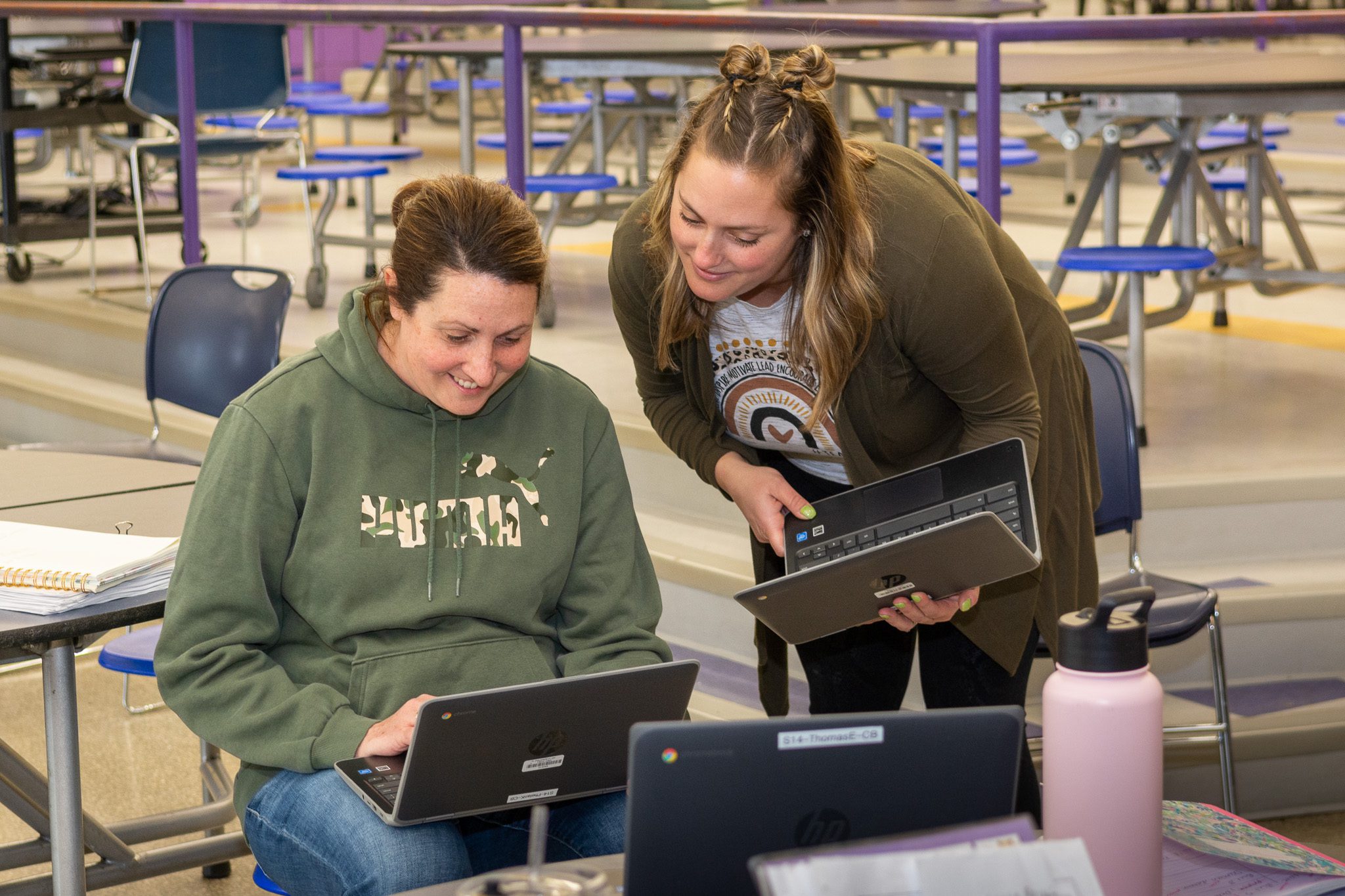 two female teachers working together with chromebooks in a school cafeteria.