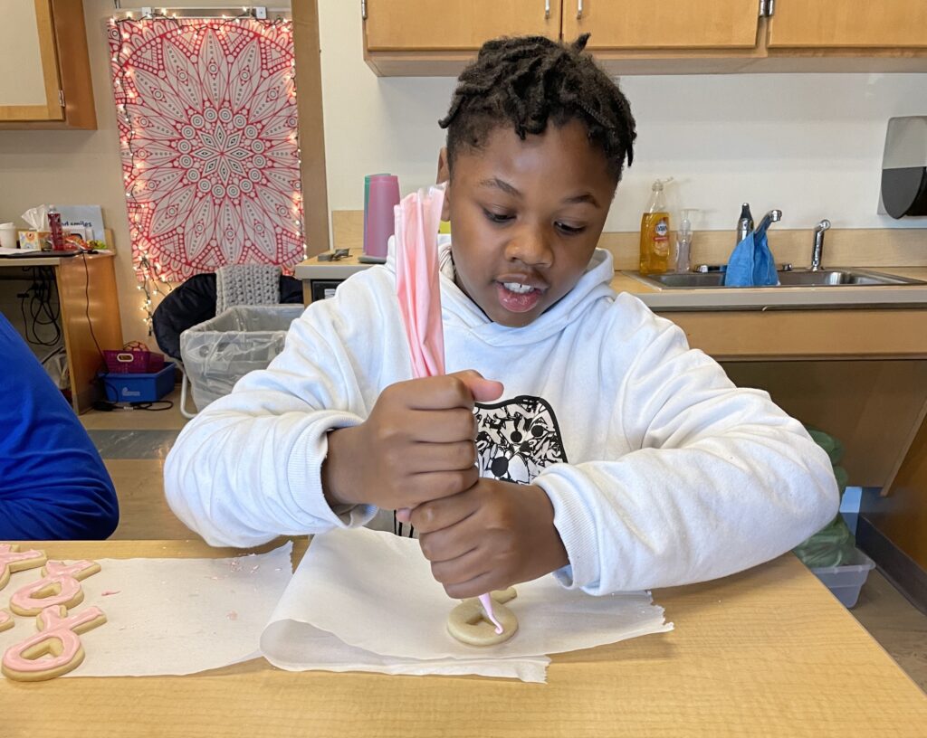 a student pipes frosting onto a cookie using a piping bag.
